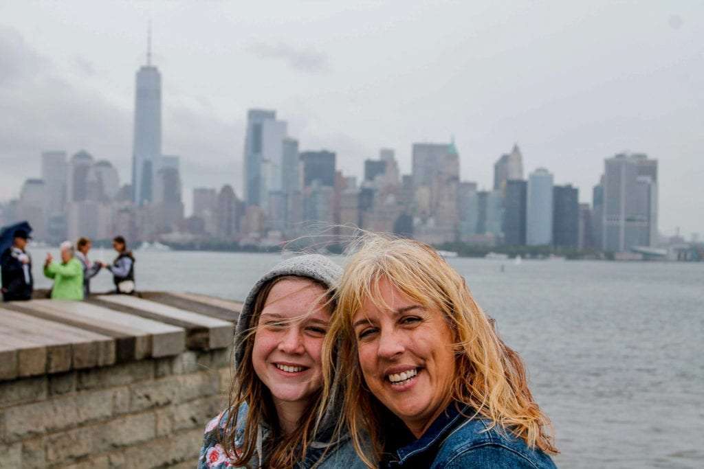 woman and child in front of the New York City skyline taken from the Statue of Liberty on a very cloudy and windy day. this was one of the best travel experiences to give your family.