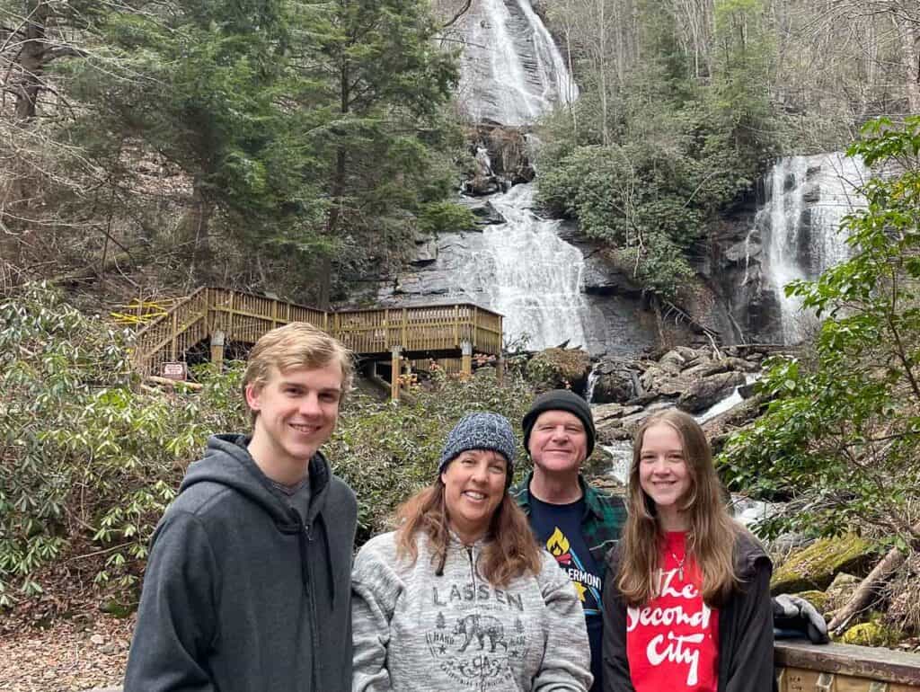 Family in front of waterfall. Son, mom, dad, daughter in winter clothing.