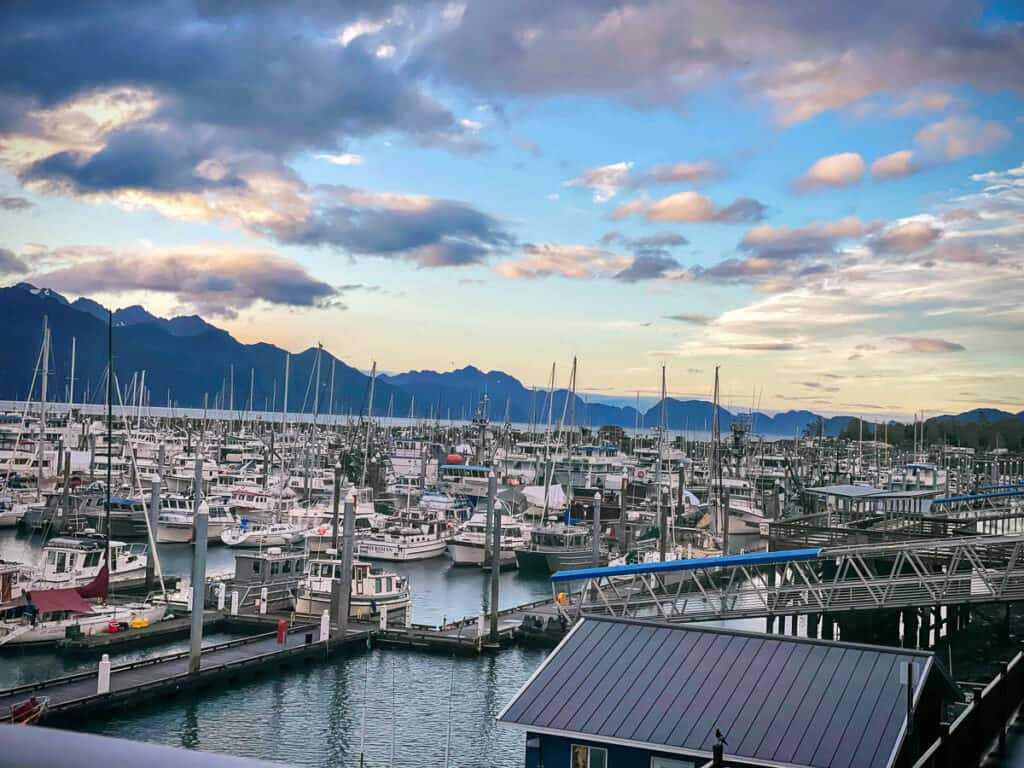 Resurrection Bay with mountains, a sunset sky, and a marina full of boats.
