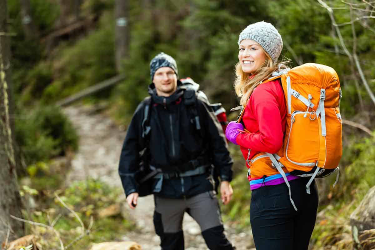 a man and woman hiking a trail. Woman has a large orange backpack and the couple are dressed warmly.