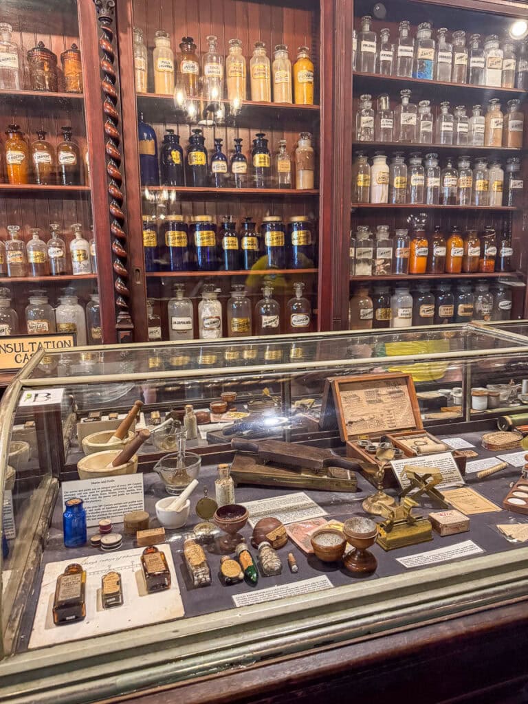 A vintage apothecary display with glass cabinets of labeled bottles and jars, plus a case of old medicinal tools and handwritten notes—an intriguing stop among New Orleans Attractions, perfect for those using the Go City New Orleans Pass to save money.