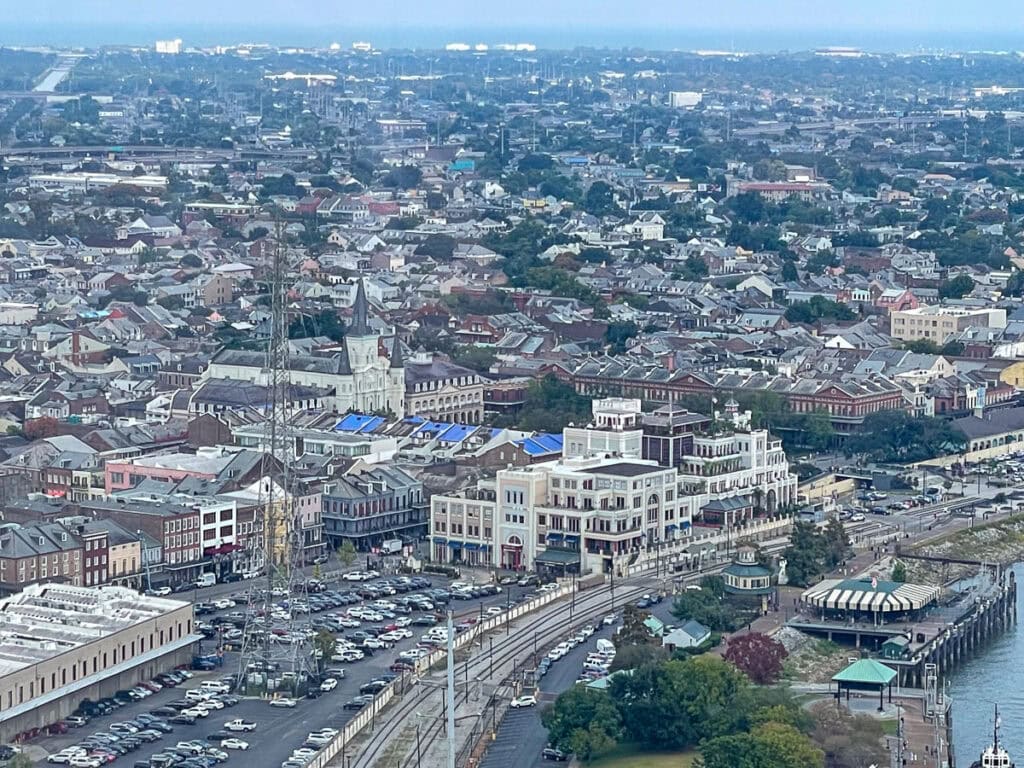 Aerial view of a city with tightly packed buildings, a church with a tall steeple, waterfront area, parked cars, and a railway line curving along the riverfront under a cloudy sky—perfect for exploring top New Orleans attractions and saving money with the Go City New Orleans Pass.