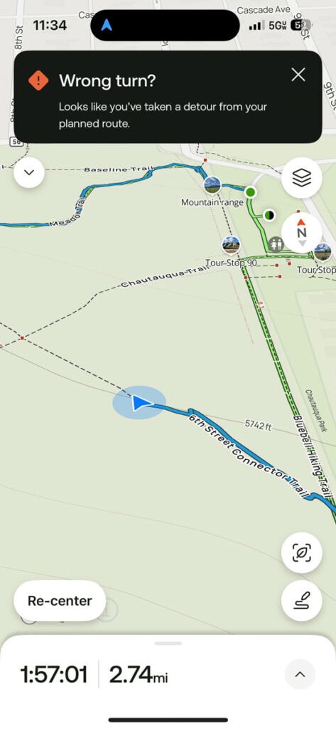 A digital map on a phone shows a blue location arrow off the main route, with a warning saying “Wrong turn? Looks like you’ve taken a detour from your planned route.” You may wonder: is AllTrails Plus worth it for better navigation? Distance and time appear below.