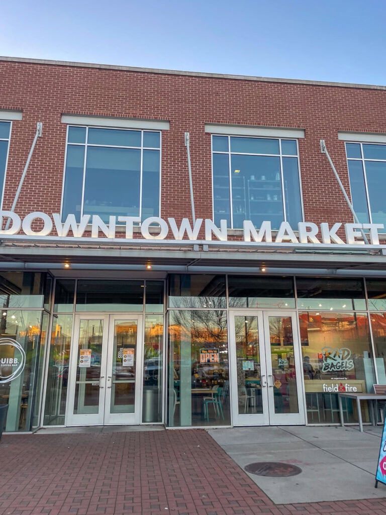 The entrance of a modern brick building with large glass windows and a sign reading "DOWNTOWN MARKET" is a must-see on any Grand Rapids itinerary. Inside, you’ll spot signs for businesses like "field & fire" and "RAD BAGELS.